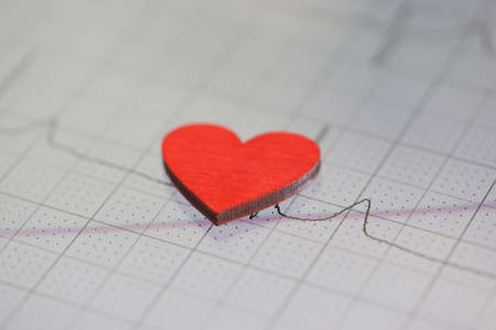 Toy red heart lying on paper with electrocardiogram closeup