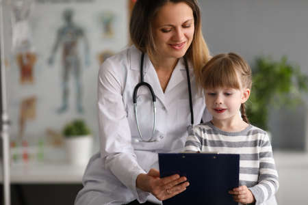 Woman pediatrician doctor communicates with girl shows card in medical officeの写真素材