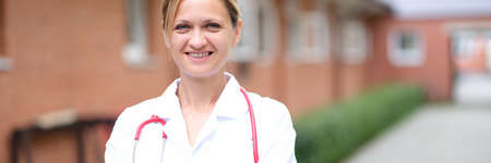 Portrait of young smiling female doctor with red stethoscope near clinicの写真素材