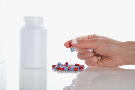 Womans hand hold one jelly capsule bunch of pill scattered on surfaceの写真素材