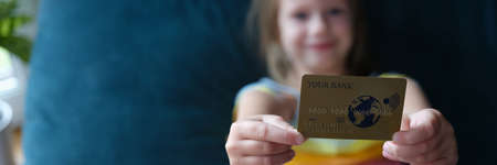 Little girl holding plastic credit bank card at home closeup