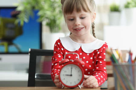 Little girl learning how to understand time and playing with red vintage clock