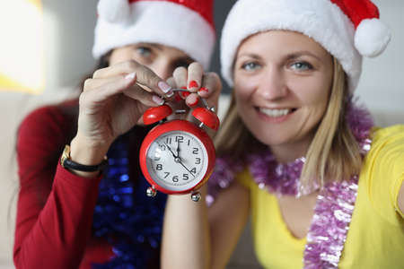 Sisters smile and hold red retro clock with arrows placed on midnightの写真素材