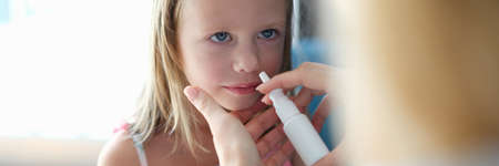 Mother sprinkling nose of little girl with vasoconstrictor drops at homeの写真素材