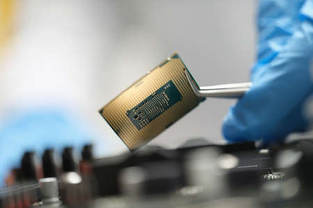 The master is holding a chip over the device with tweezers, close-upの写真素材