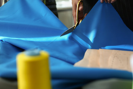 Atelier worker cutting blue cloth with scissors for further sewingの写真素材