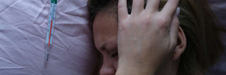 Young woman in bed and holding her head near mercury thermometer