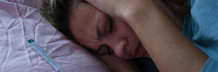 Woman lying in bed and holding sore head with hands near mercury thermometerの写真素材