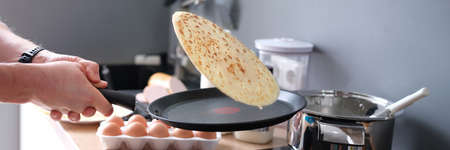 Male chef tossing pancake in frying pan in kitchen closeupの写真素材