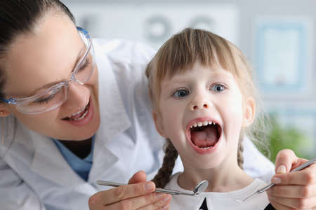 Cute kid visiting family doctor and open mouth pediatrician with tool check hurting throat