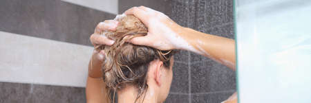 Young woman washing her hair with shampoo in showerの写真素材