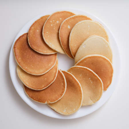 Plate with many round pancakes standing on white background top view