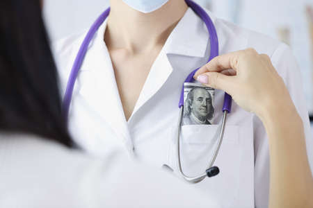 Woman patient put banknote in doctors pocket on appointment for better serviceの写真素材