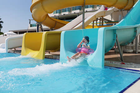 Happy little girl kid slide down hill on pink air mattress in water park
