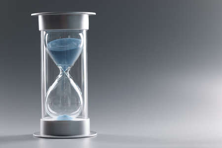 Closeup of hourglass with blue sand on gray backgroundの写真素材