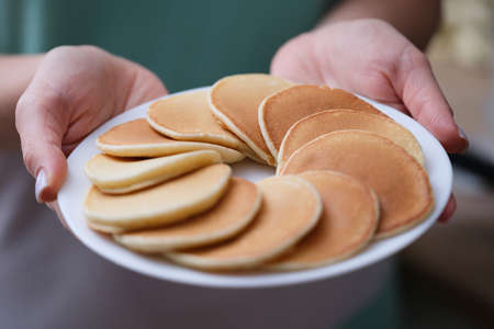 Round appetizing flour pancakes on white plate in female handsの写真素材
