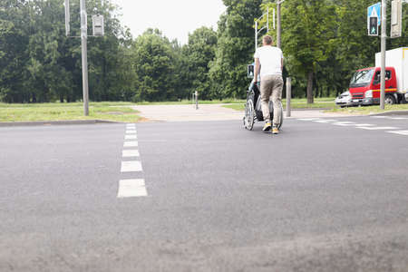 Man drive woman on wheelchair across street at pedestrian crossingの写真素材