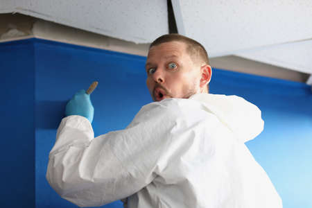 Male worker caught by surprise painting wall in blue colourの写真素材