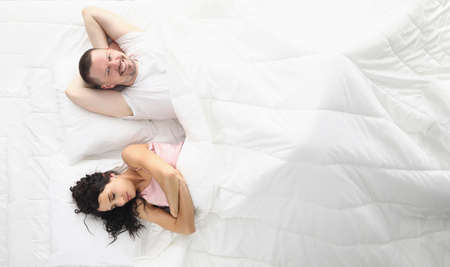 Wife and husband happily laying bed, white bedclothesの写真素材