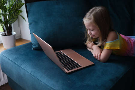 A little girl is lying on the couch with a laptopの写真素材