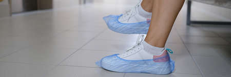 Women legs in sneakers with shoe covers in hospital corridor
