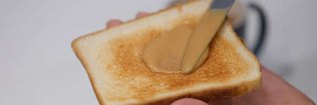 Woman spreads peanut butter on toast with knife closeupの写真素材