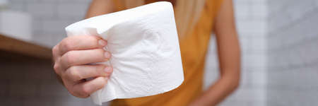 Woman is sitting on t toilet and holding roll of toilet paper