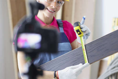 Smiling woman construction site worker measure plank with tape measure toolの写真素材