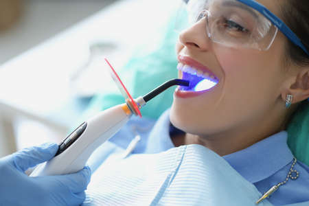 Female in stomatology cabinet seat getting whitening procedure, open mouth widelyの写真素材