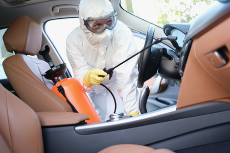 Hazmat female worker cleanse car interior with spray disinfectanの写真素材