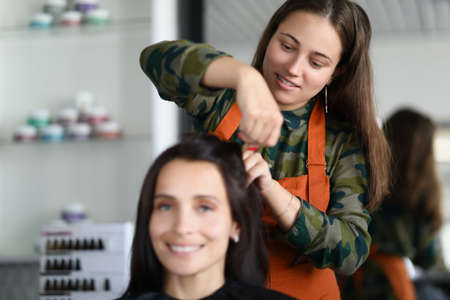 Smiling hairdresser creating fancy hairstyle for female clientの写真素材