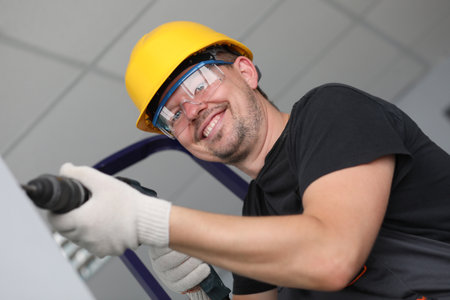 Smiling builder in helmet drilling wall in house