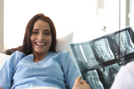 Doctor holding xray of spine in front of smiling female patient