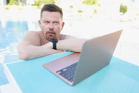 Annoyed man working on a laptop from the poolの写真素材