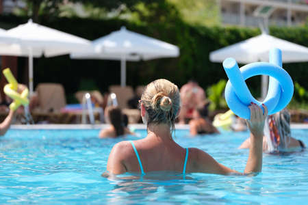Woman in the pool doing exercises in aquafitness, back view
