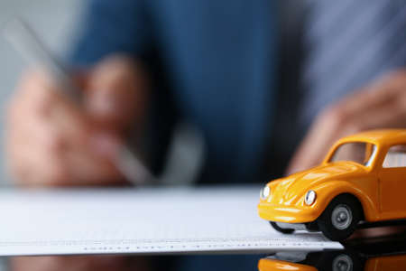 Car insurance paper on desk, yellow auto miniature on document