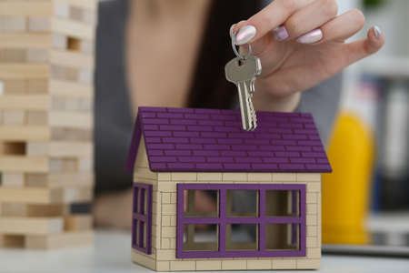Female worker hand hold key to unlock new miniature toy house, buy new accommodationの写真素材