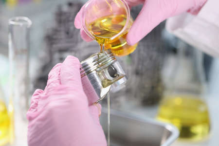 Mans hand in rubber gloves holding car part and pours lubricating oil on itの写真素材
