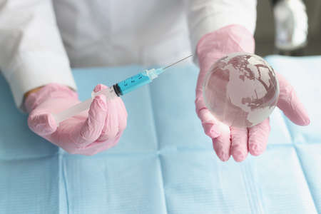 Medical worker hold syringe and miniature world globe in handsの写真素材
