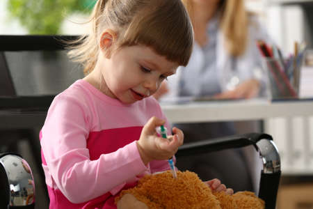 Little girl gives injection to toy closeupの写真素材