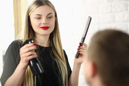 Hairdresser holding comb and spray with water in front of male client in beauty salonの写真素材