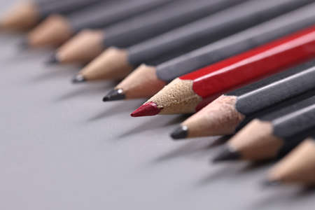 Closeup of one red wooden pencil among many black backgroundの写真素材