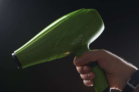 Male hand holding green hair dryer on black background closeup