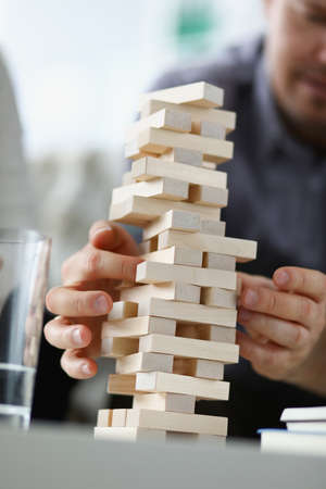 Young man removing wooden blocks from toy tower closeup