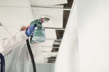 Male construction worker in protective overalls painting wall white with spray gun closeupの写真素材