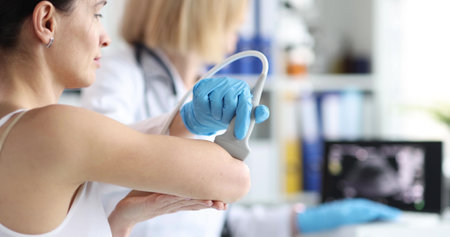 Doctor conducting ultrasound examination of patient elbow in clinic closeupの写真素材