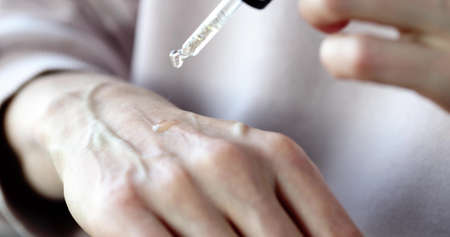 Woman applying drop of anti-aging serum oil with apipette to hand closeupの写真素材