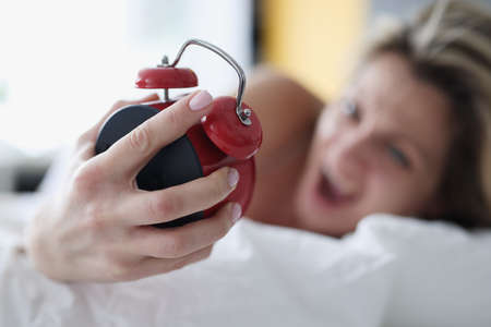 Screaming woman in bed with a red alarm clock in her handの写真素材