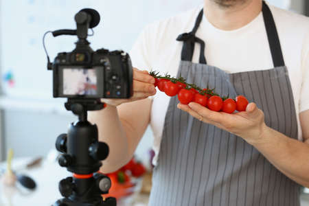 Vlogger chef showing ripe tomatoes ingredient, man in apron recording red vegetableの写真素材