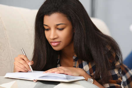 Mulatto girl on the sofa makes notes in the book, close-up